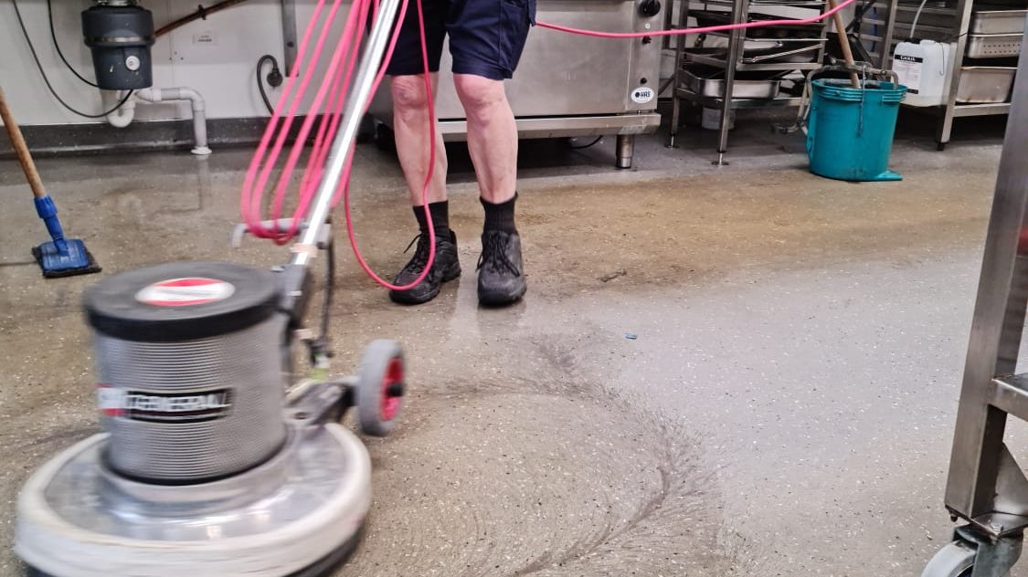 Our cleaner scrubbing a commercial kitchen floor with a floor machine